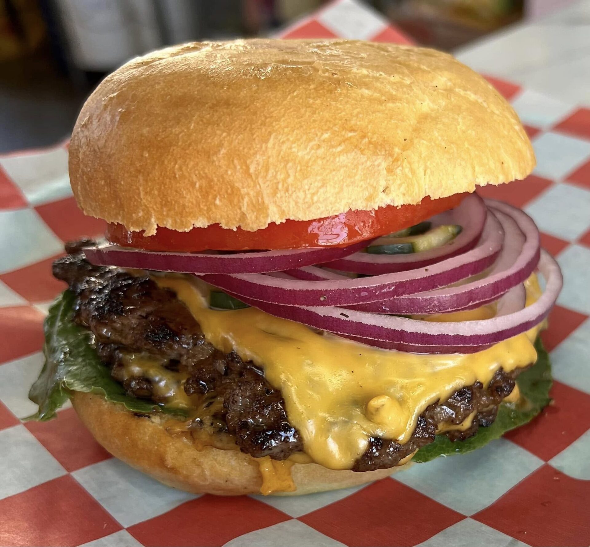 V9 Smash Burger with melted cheese, red onion and tomato on red-and-white checkered paper