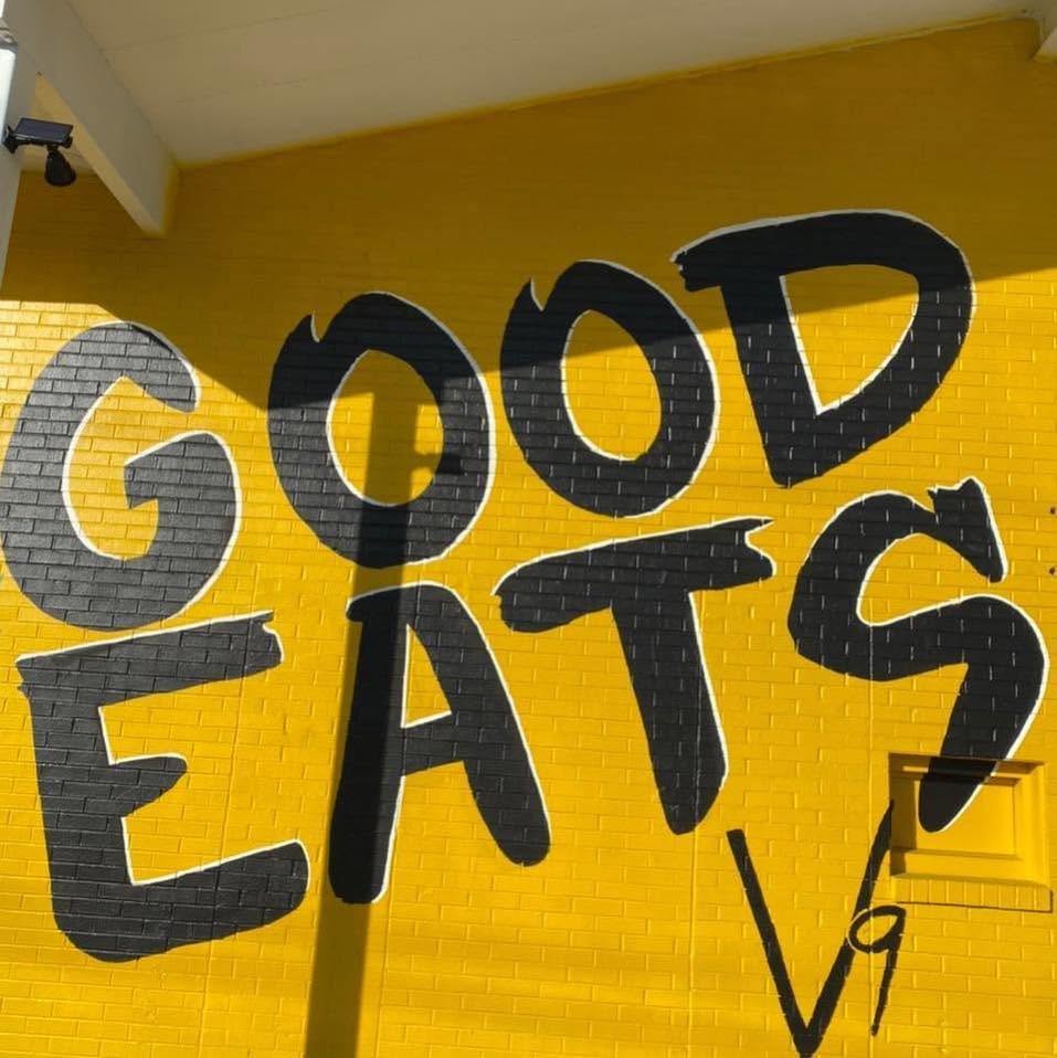 The hand-painted GOOD EATS mural on V9's sunflower-yellow wall