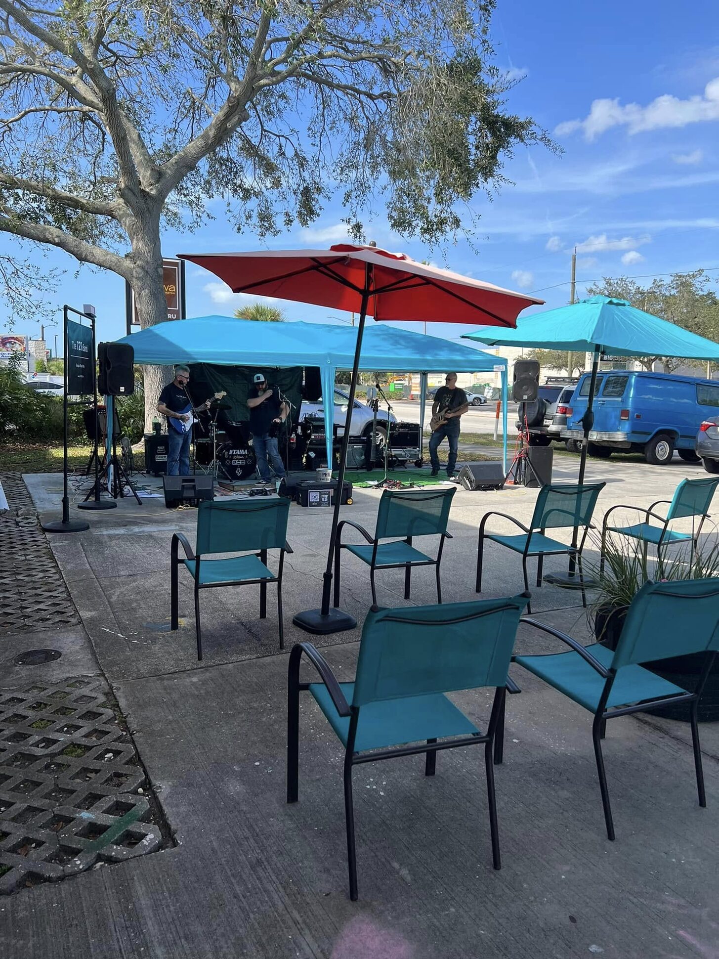 Patio chairs under teal umbrellas beside the oak